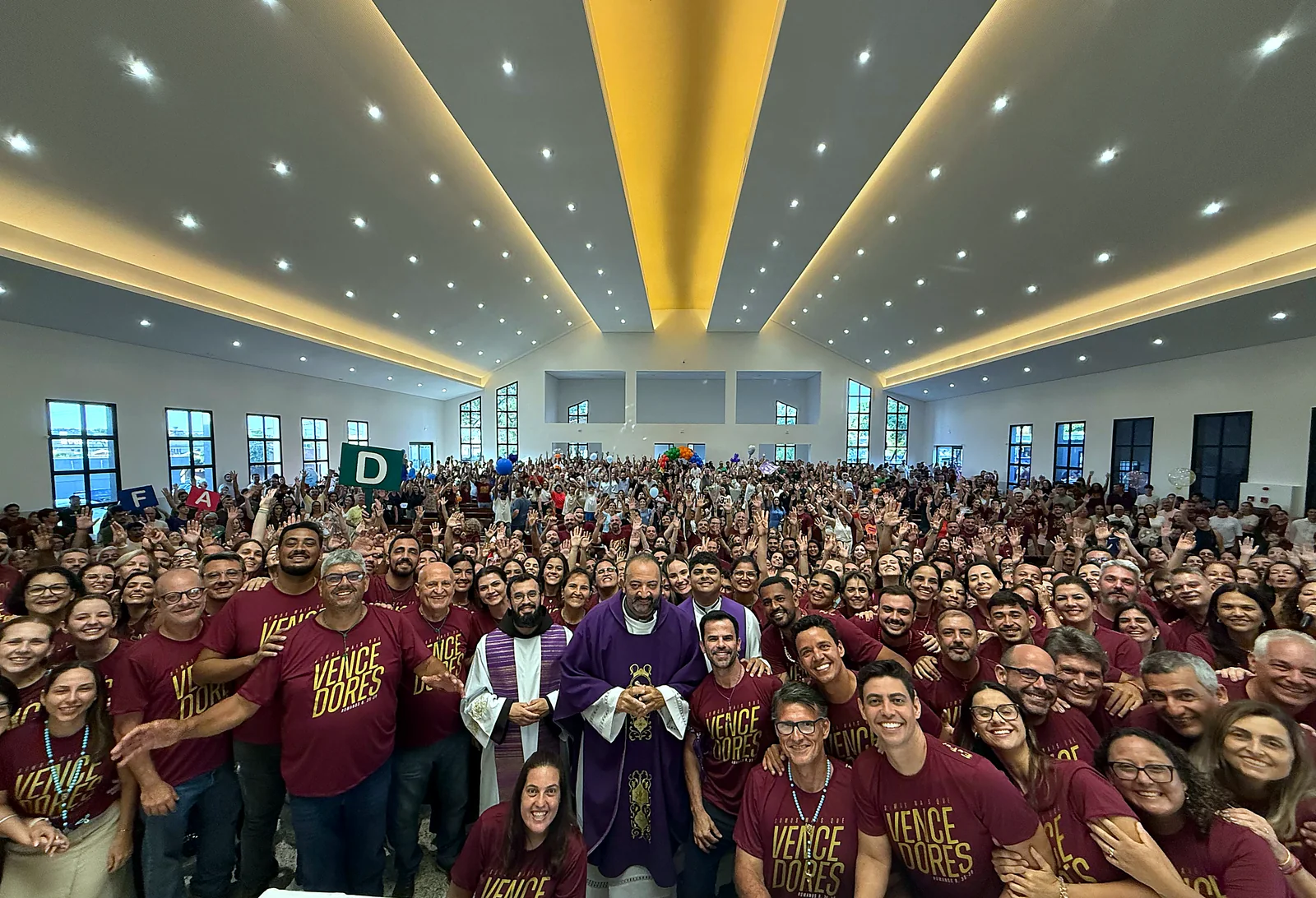 Salão lotado em evento católico com camisetas personalizadas